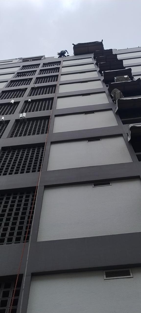 Profissional em rapel pintando a fachada de um edifício