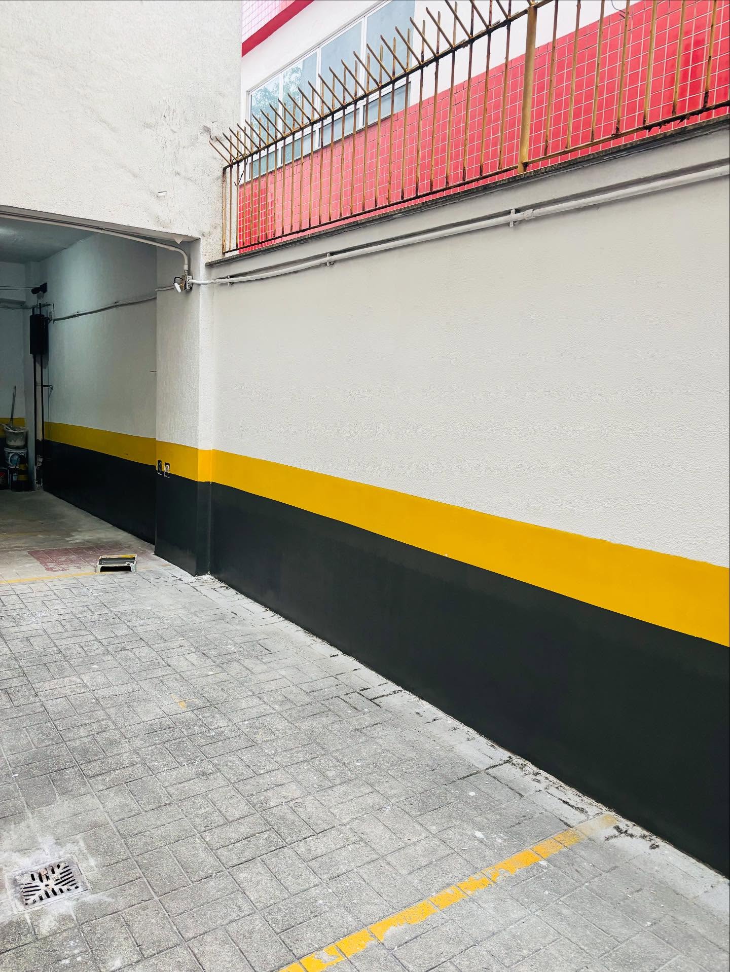 Parede predial pintada com faixa amarela e rodapé escuro