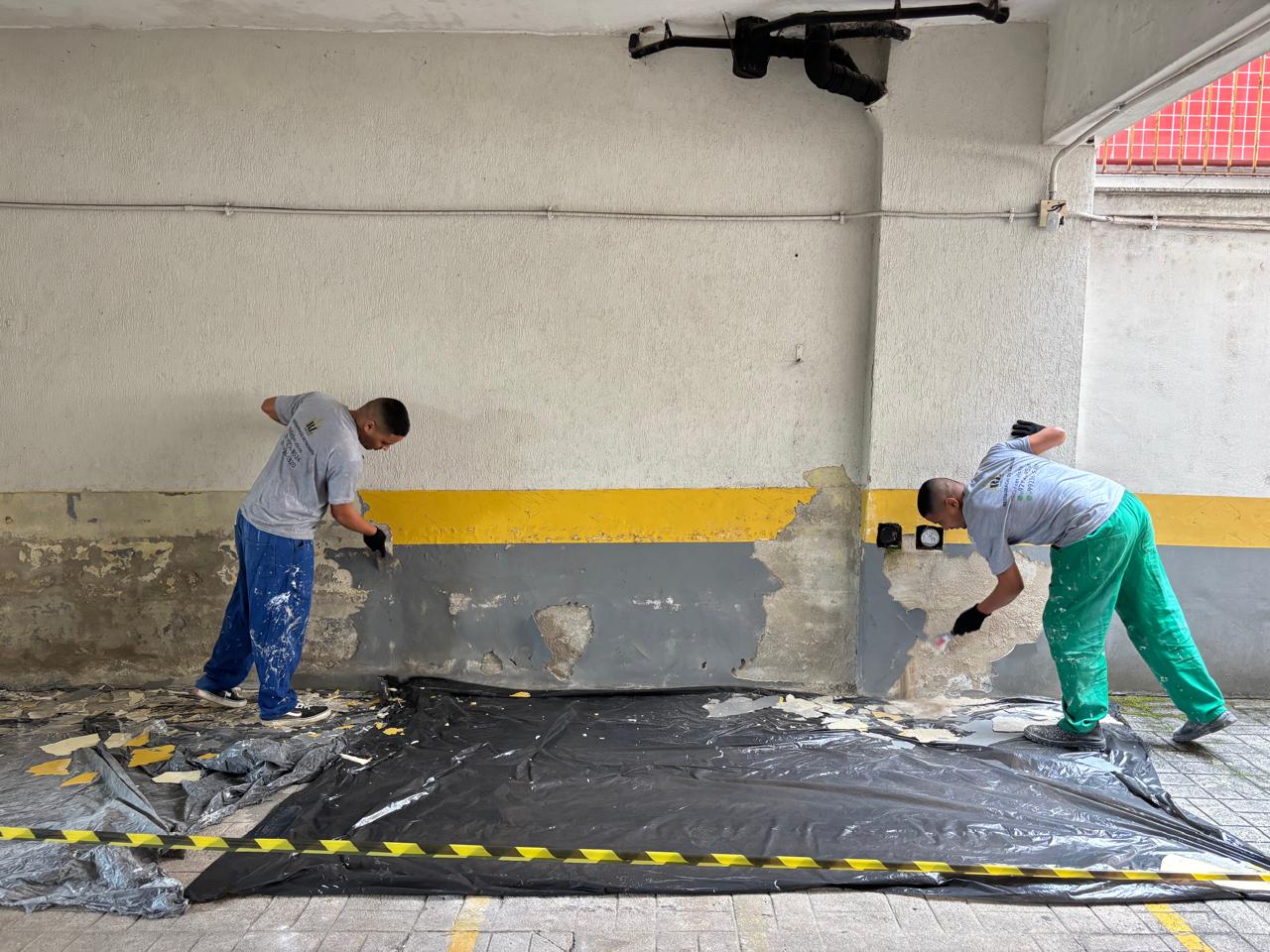 Dupla de profissionais raspando reboco danificado em garagem